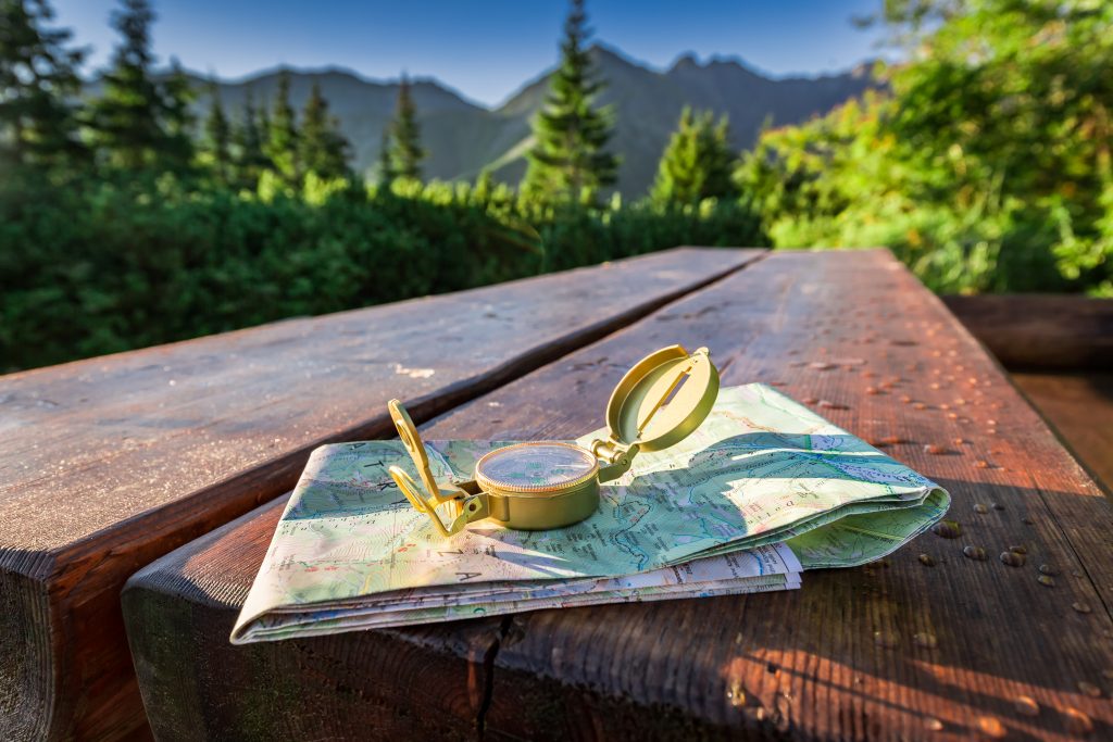 Compass and folded map on wooden picnic table in the outdoors with surrounding trees