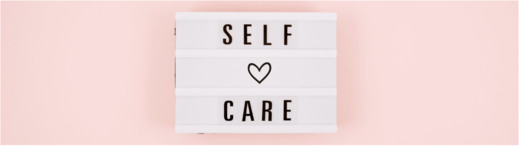 text board with words self care and a heart symbol behind a pink background