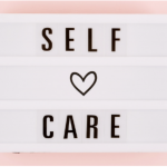 text board with words self care and a heart symbol behind a pink background